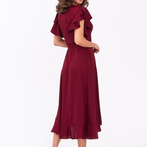 May include: A burgundy midi dress with a wrap style and ruffled sleeves. The dress has a fitted bodice and a flowing skirt with a ruffled hem.