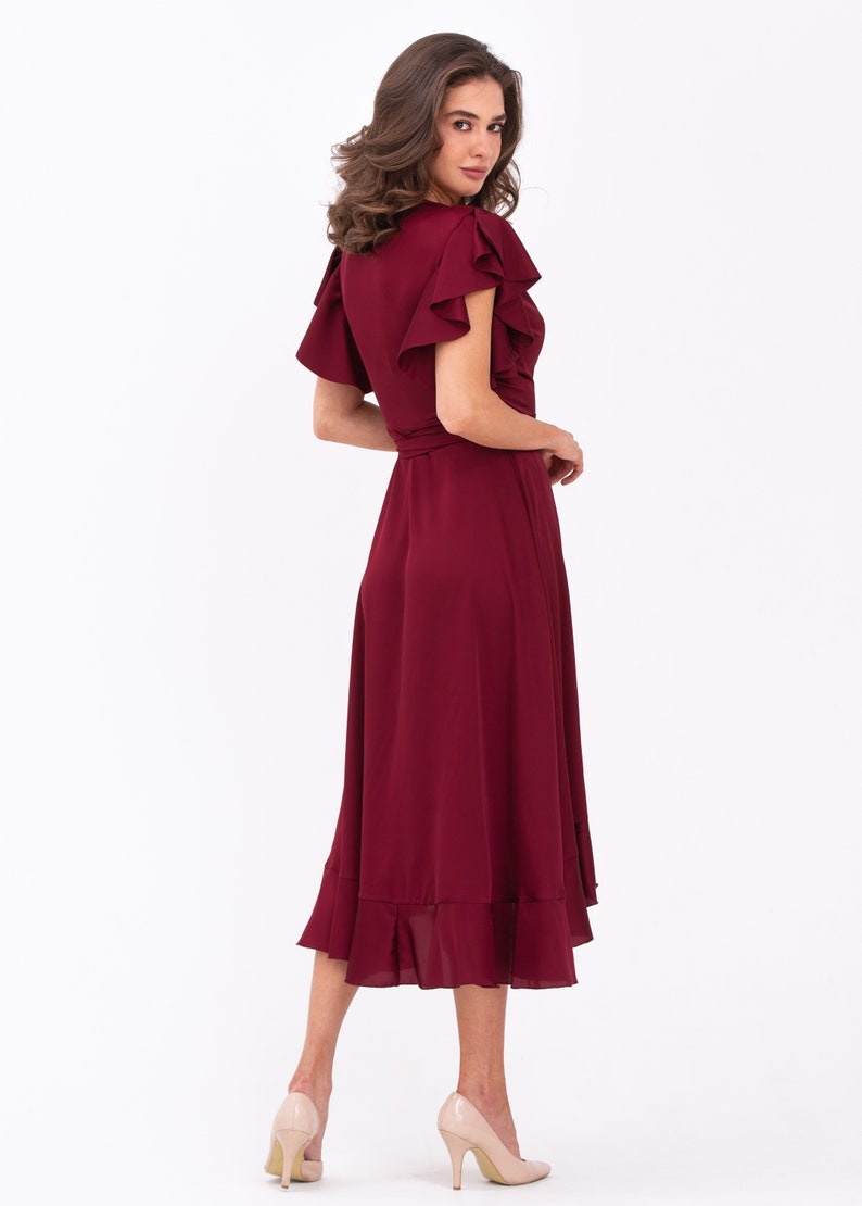 May include: A burgundy midi dress with a wrap style and ruffled sleeves. The dress has a fitted bodice and a flowing skirt with a ruffled hem.