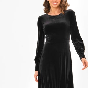 May include: A black velvet dress with long sleeves and a round neckline. The dress has a fitted bodice and a flowing skirt.