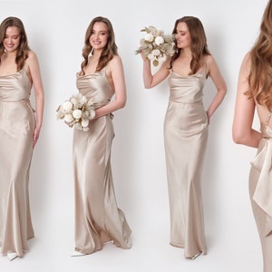 May include: Three women wearing long, champagne-colored satin dresses. The dresses have a cowl neckline and a fitted bodice. The dress on the right has a large bow in the back. The women are holding bouquets of dried flowers.