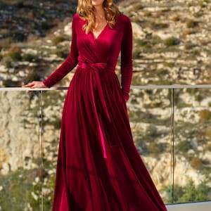 K&ouml;nnte beinhalten: Ein lang&auml;rmeliges, burgunderfarbenes Samt-Wickelkleid mit V-Ausschnitt und einem passenden G&uuml;rtel, der in der Taille gebunden ist.