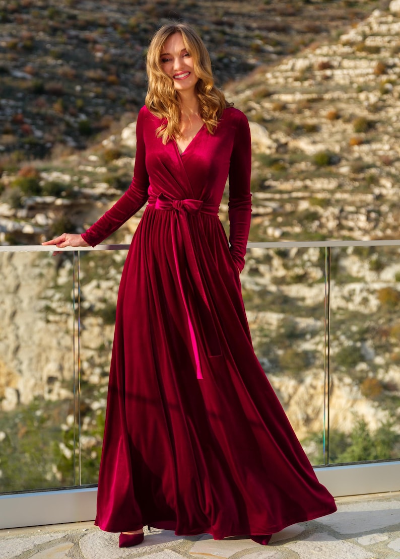 K&ouml;nnte beinhalten: Ein lang&auml;rmeliges, burgunderfarbenes Samt-Wickelkleid mit V-Ausschnitt und einem passenden G&uuml;rtel, der in der Taille gebunden ist.