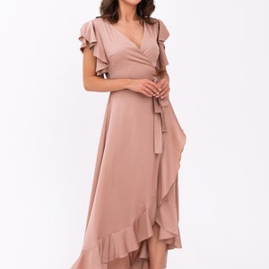 May include: A long, flowing, blush-coloured wrap dress with a ruffled hem and short, ruffled sleeves. The dress has a V-neckline and a tie at the waist.