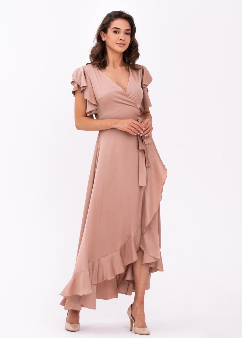 May include: A long, flowing, blush-coloured wrap dress with a ruffled hem and short, ruffled sleeves. The dress has a V-neckline and a tie at the waist.