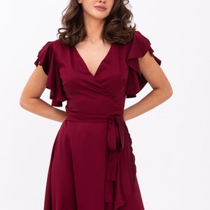 May include: A burgundy wrap dress with short sleeves and a ruffled hem. The dress has a V-neckline and a tie at the waist.