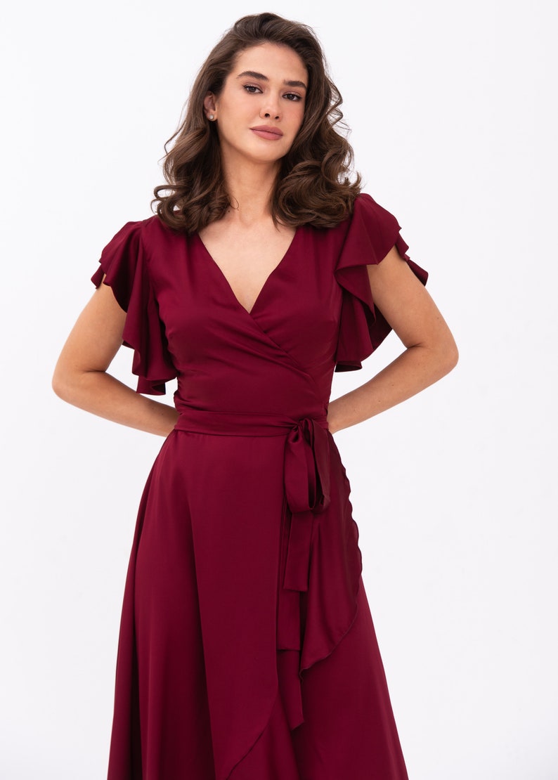 May include: A burgundy wrap dress with short sleeves and a ruffled hem. The dress has a V-neckline and a tie at the waist.