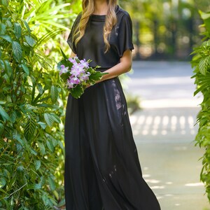 May include: A woman in a black top and matching wide-leg pants holds a bouquet of pink and white orchids.