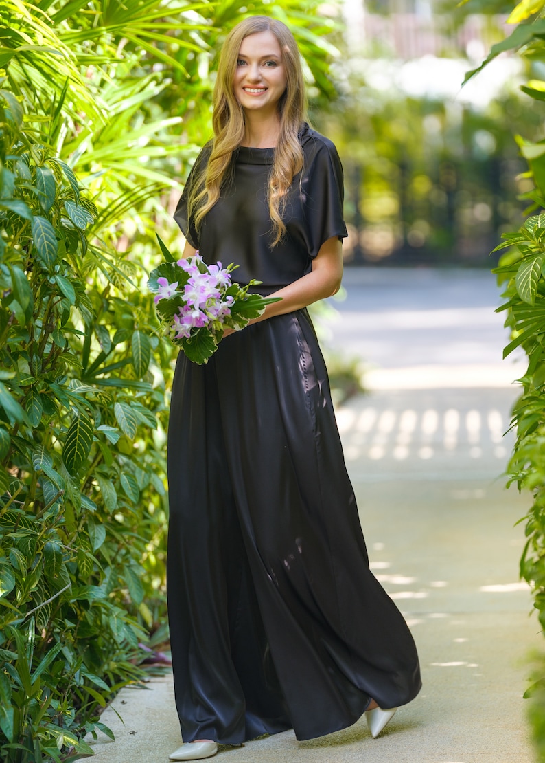 May include: A woman in a black top and matching wide-leg pants holds a bouquet of pink and white orchids.