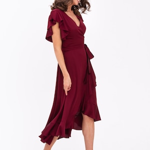 May include: A burgundy wrap dress with short ruffled sleeves and a high low hemline. The dress has a tie at the waist and is made of a soft, flowing fabric.