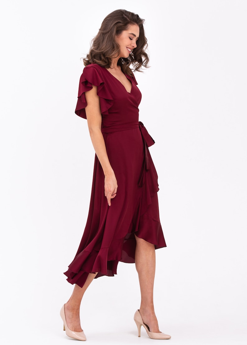 May include: A burgundy wrap dress with short ruffled sleeves and a high low hemline. The dress has a tie at the waist and is made of a soft, flowing fabric.