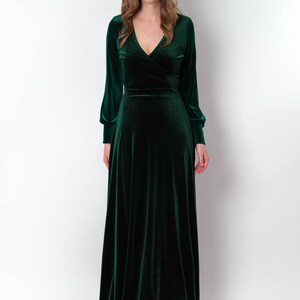K&ouml;nnte beinhalten: Ein langes, smaragdgr&uuml;nes Samtkleid mit V-Ausschnitt und langen &Auml;rmeln. Das Kleid hat einen Wickel-Oberteil und einen flie&szlig;enden Rock.