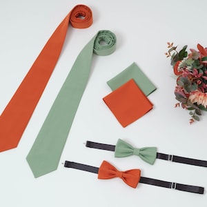 May include: Two neckties, one orange and one green, with a matching pocket square and two bow ties. The bow ties are also orange and green.