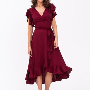 May include: A burgundy wrap dress with short ruffle sleeves and a high-low hemline. The dress has a tie at the waist and a ruffled skirt.