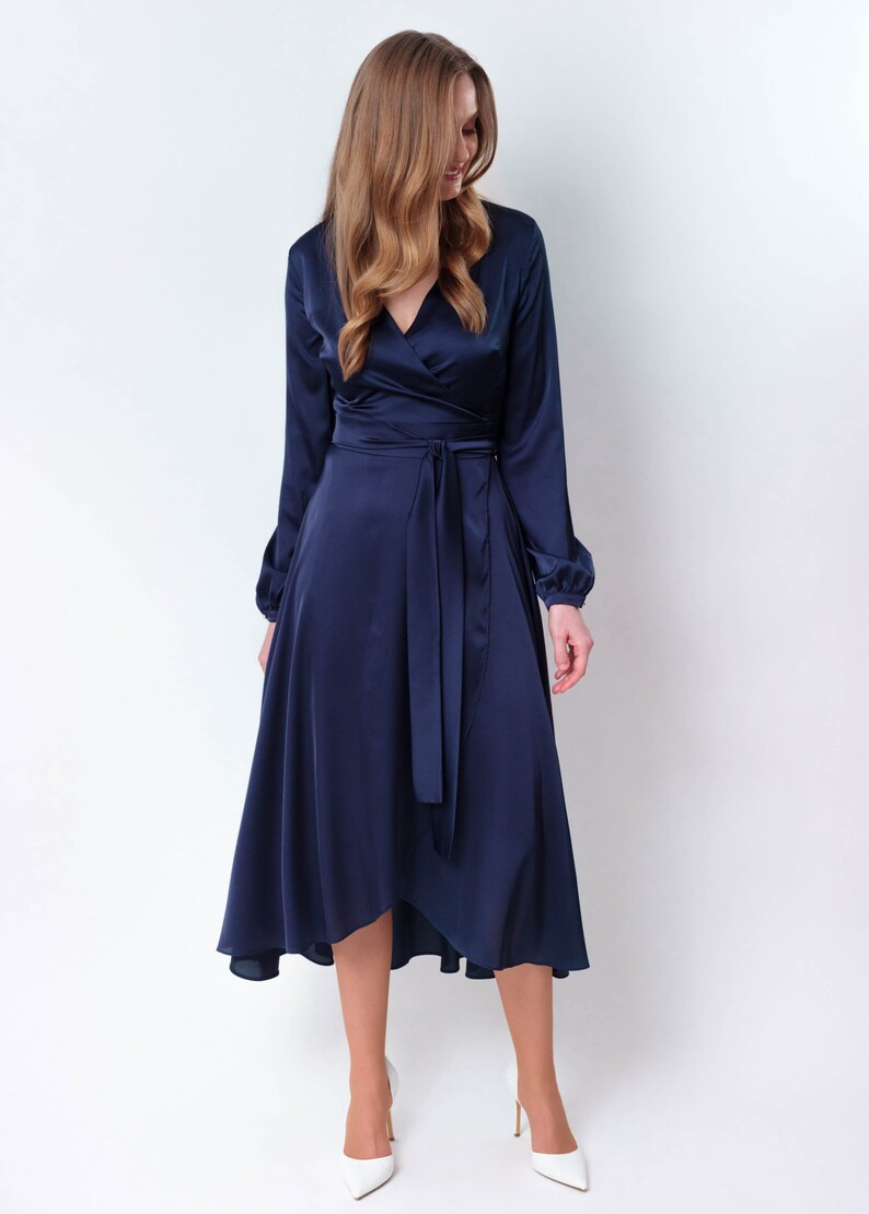 May include: A navy blue satin wrap dress with long sleeves and a tie at the waist. The dress has a high neckline and a high-low hemline.