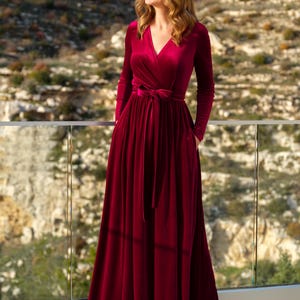 K&ouml;nnte beinhalten: Ein lang&auml;rmeliges, burgunderfarbenes Samt-Wickelkleid mit einer Schleife in der Taille.