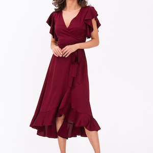 May include: A burgundy wrap dress with short ruffle sleeves and a ruffled hem. The dress has a tie at the waist.