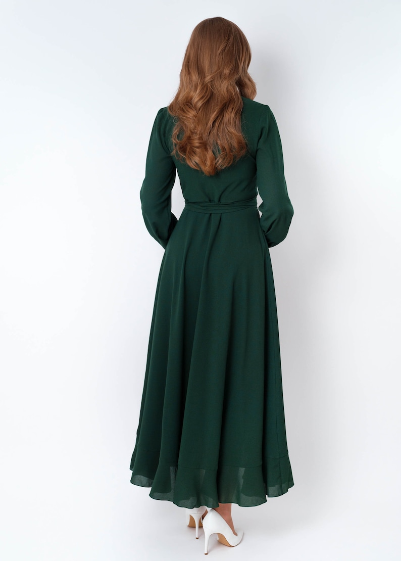 May include: A long, dark green maxi dress with a wrap style bodice and long sleeves. The dress has a ruffled hem and is cinched at the waist with a matching belt.
