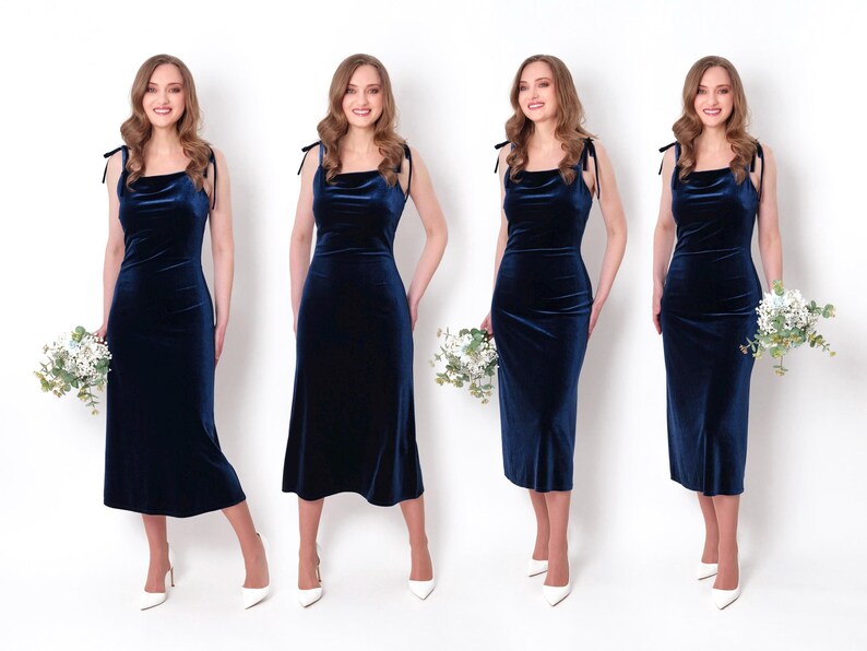 May include: Four women wearing navy blue velvet dresses with thin straps and a cowl neckline. Each woman is holding a bouquet of white flowers and is wearing white heels.