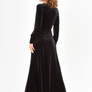 May include: A long black velvet dress with a V-neckline and long sleeves. The dress has a wrap-style design and a belt at the waist.