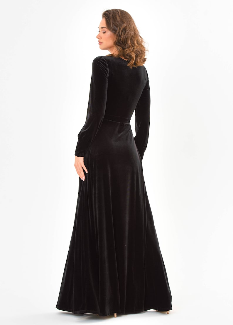 May include: A long black velvet dress with a V-neckline and long sleeves. The dress has a wrap-style design and a belt at the waist.