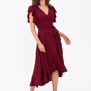 May include: A burgundy wrap dress with short ruffle sleeves and a ruffled hem. The dress has a tie belt at the waist.