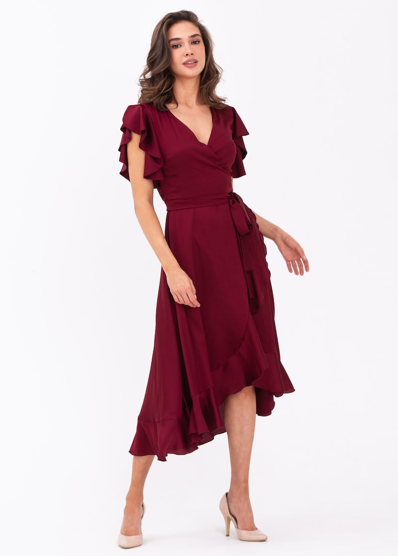 May include: A burgundy wrap dress with short ruffle sleeves and a ruffled hem. The dress has a tie belt at the waist.