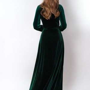 K&ouml;nnte beinhalten: Ein langes, dunkelgr&uuml;nes Samtkleid mit Wickeloptik und langen &Auml;rmeln. Das Kleid ist flie&szlig;end und hat einen leichten Glanz.