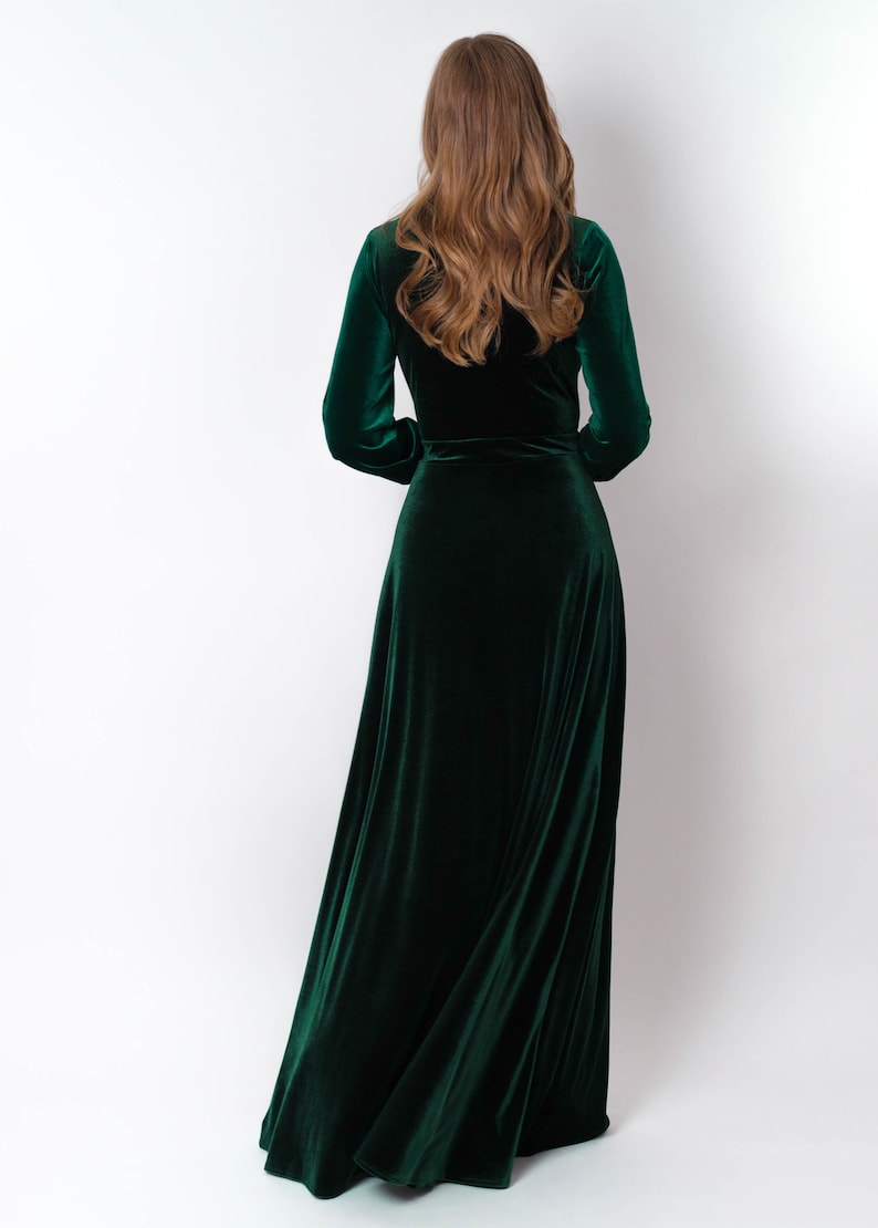 K&ouml;nnte beinhalten: Ein langes, dunkelgr&uuml;nes Samtkleid mit Wickeloptik und langen &Auml;rmeln. Das Kleid ist flie&szlig;end und hat einen leichten Glanz.