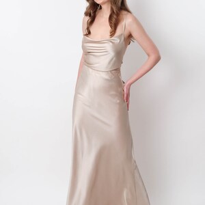 May include: A woman wearing a long, flowing, champagne-colored satin dress with a cowl neck and spaghetti straps.