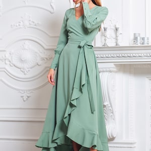 May include: A sage green wrap dress with long sleeves and a ruffled hem. The dress has a tie belt at the waist and a V-neckline.
