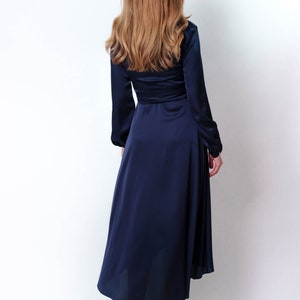 May include: A long, navy blue satin dress with long sleeves and a wrap-style bodice. The dress has a high neckline and a flowing skirt.