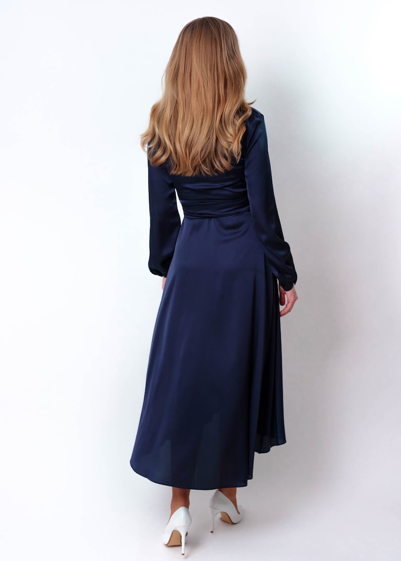 May include: A long, navy blue satin dress with long sleeves and a wrap-style bodice. The dress has a high neckline and a flowing skirt.