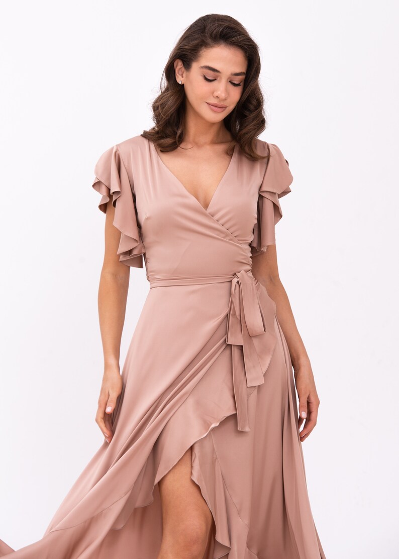 May include: A long, flowing, blush-coloured wrap dress with a V-neckline, ruffled sleeves, and a tie at the waist.