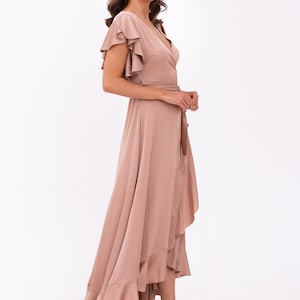 May include: A long, flowing, blush-coloured wrap dress with a ruffled hem and short, ruffled sleeves. The dress has a V-neckline and a tie at the waist.