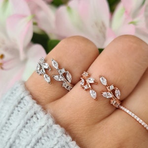 Op de afbeelding: Twee delicate ringen met een bladontwerp met heldere zirkonia-stenen. De ring aan de linkerkant is zilver, en de ring aan de rechterkant is roségoud.
