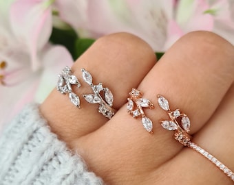 May include: Two delicate rings with a leaf design featuring clear cubic zirconia stones. The ring on the left is silver, and the ring on the right is rose gold.
