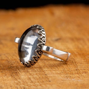 May include: A silver ring with a clear oval-shaped gemstone set in a decorative silver bezel. The ring has a simple band.