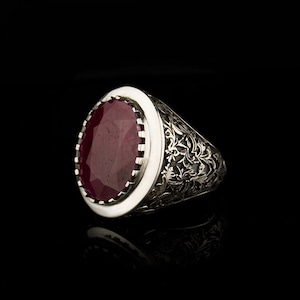 Peut inclure: Une bague en argent avec une pierre précieuse de rubis de forme ovale sertie dans un motif de filigrane décoratif.
