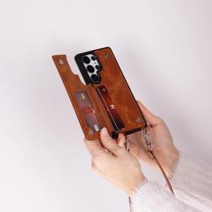 May include: A brown leather phone case with a card slot and a detachable strap. The case is open to reveal a credit card inside the slot.