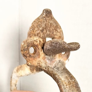 May include: A rusty metal door handle with a latch. The handle is shaped like a loop and has a white, powdery coating.