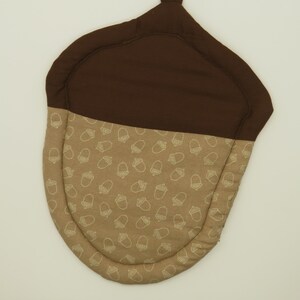 May include: Brown and tan acorn-shaped oven mitt with a loop handle. The mitt is decorated with a white acorn pattern.