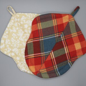 May include: Two pot holders, one with a white floral pattern and one with a red, green, and blue plaid pattern.