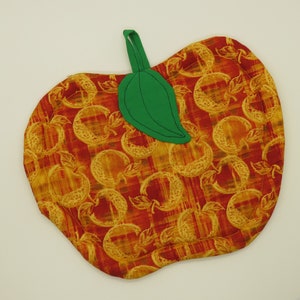 May include: Apple-shaped quilted potholder with a green leaf and loop. The fabric features a repeating pattern of apples in shades of red, orange, and yellow. The potholder is designed to protect surfaces from heat.