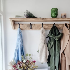 May include: A rustic wooden coat rack with five hooks and a shelf. The rack is mounted on a white wall and has a variety of coats and jackets hanging from it. There is a small framed photo of two children on the shelf below the rack.