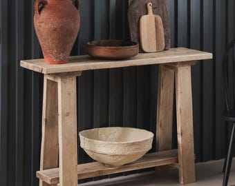 May include: A rustic wooden console table with a natural finish. The table has a single shelf and two A-frame legs. A terracotta pot with a plant, a wooden bowl, and a paper bowl are on the table.