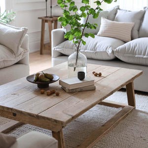 May include: A rustic wooden coffee table with a natural finish. The table has a rectangular top and a simple, sturdy design. It is decorated with a bowl of pears, a vase of greenery, and a stack of books.