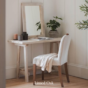 May include: A white wooden vanity table with a mirror and a white chair. The table has a shelf underneath and is made of reclaimed wood. The chair is upholstered in a white fabric. The table is labelled "Limed Oak".