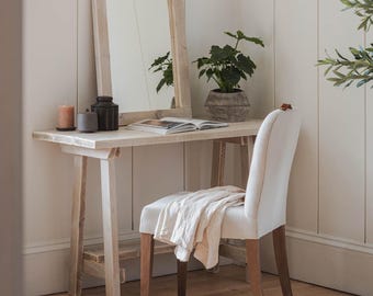 May include: A white wooden vanity table with a mirror and a white chair. The table has a shelf underneath and is made of reclaimed wood. The chair is upholstered in a white fabric. The table is labeled "Limed Oak".