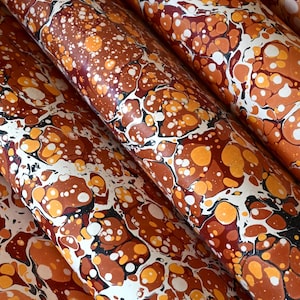 May include: A collection of rolled sheets of paper featuring a marbled pattern in shades of deep rust, burnt orange, bright yellow, and white, with thin black veins separating the organic, rounded shapes across the entire surface area.