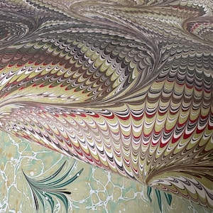 May include: A sheet of paper featuring two distinct marbled patterns. The top section displays a dense, repeating wave design in shades of brown, red, white, and gold. The bottom section shows a light green marbled pattern with dark green accents.